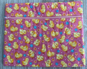May include: A quilted pink zippered pouch featuring a repeating pattern of yellow chicks, blue flowers, and white dots. The pouch has a pink zipper and a quilted design. The overall theme is spring or Easter.