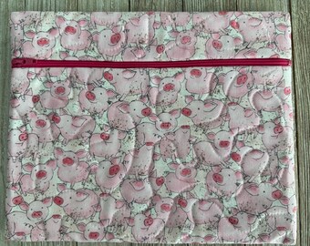 May include: A square quilted fabric pouch featuring an all-over print of cartoon pink pigs on a white background. The pouch is secured with a horizontal dark pink zipper that runs across the upper third of the item.