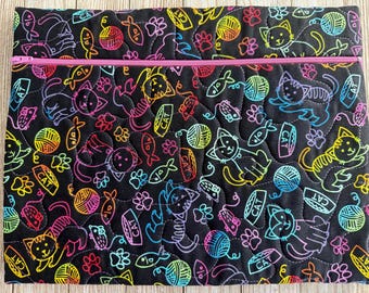 May include: A rectangular quilted fabric pouch featuring a black background with a colorful neon-style print of cats, yarn balls, fish, and paw prints. The pouch includes a bright pink horizontal zipper closure across the top section.
