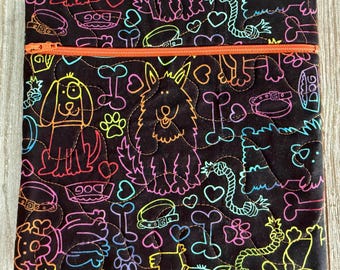May include: A square quilted fabric pouch with a black background featuring a colorful neon-style print of dogs, bones, hearts, collars, and rope toys. The pouch includes a horizontal orange zipper closure across the top section of the item.