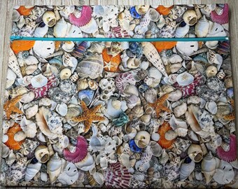 May include: A rectangular fabric pouch featuring a dense, colorful print of various seashells, starfish, and sand dollars. The pouch is secured at the top with a bright teal zipper that spans the entire width of the item.