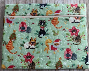May include: A rectangular quilted pouch in light green featuring a repeating pattern of cats dressed in holiday attire, including Santa hats, reindeer antlers, and Christmas tree costumes, with a silver zipper closure along the top edge.