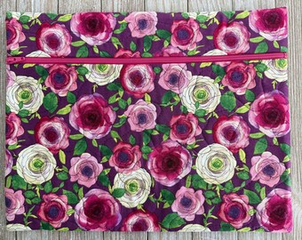 May include: A quilted fabric case with a vibrant floral pattern. The design features large roses in shades of pink, white, and burgundy against a deep purple background. A bright pink zipper runs across the top.