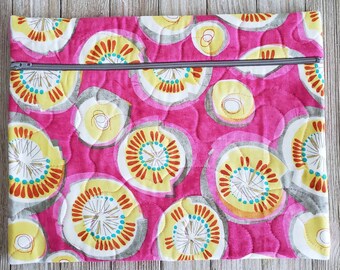 May include: A pink quilted zippered pouch with a colorful floral pattern. The pouch has a zipper closure and is made of a soft, quilted fabric.