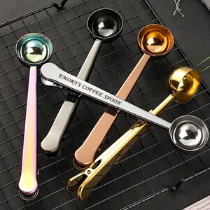 May include: Four stainless steel coffee measuring spoons with clips. The spoons are in different colors: silver, gold, rose gold, and iridescent. The spoons have the words "Emory's Coffee Spoon" engraved on the handle.