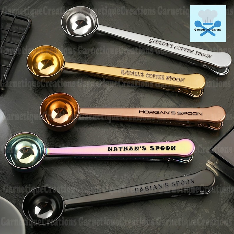 May include: Five personalized coffee spoons with clips. The spoons are silver, gold, rose gold, iridescent, and black. Each spoon has a name engraved on it: Gideon's Coffee Spoon, Rafael's Coffee Spoon, Morgan's Spoon, Nathan's Spoon, and Fabian's Spoon.