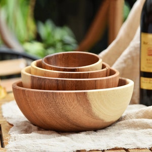 May include: Set of four wooden bowls, nested together, made of light and dark brown wood. The bowls are round and have a smooth, polished finish.