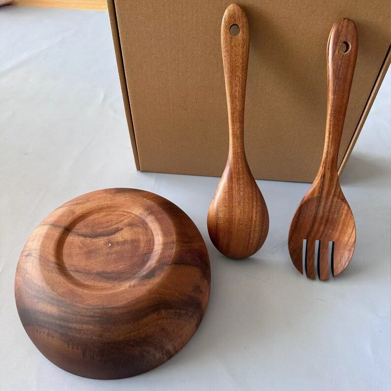 May include: A set of wooden serving utensils, including a bowl, spoon, and fork. The utensils are made of dark brown wood and have a natural, rustic look.