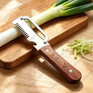 May include: A stainless steel and wood vegetable peeler with a serrated blade and bottle opener. The wooden handle is engraved with the name "William" and a heart. A leek and cut leek are on a wooden cutting board.