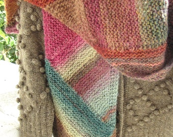 May include: A brown knitted shawl with a multi-colored striped pattern in shades of orange, pink, teal, and cream. The shawl is draped over a brown knitted jacket with textured buttons.