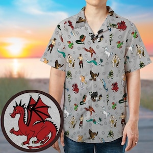 Può includere: Una camicia a maniche corte, abbottonata, con sfondo grigio chiaro e un motivo ripetuto di varie creature fantasy in più colori. Un drago rosso è presente in un emblema circolare in basso a sinistra. La camicia è indossata.