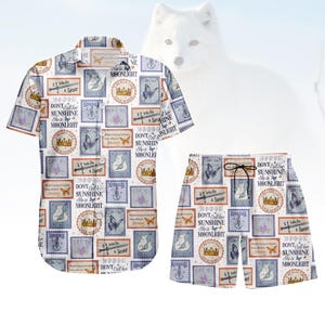 Könnte beinhalten: Ein zweiteiliges Set, bestehend aus einem kurzärmeligen Hemd und Shorts. Das Set ist weiß mit einem sich wiederholenden Muster aus Briefmarken-ähnlichen Designs in Blau, Lila und Gold, mit dem Text "DON'T Call her SUNSHINE She is MOONLIGHT".