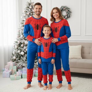 May include: A family of three wearing matching Spider-Man pajamas. The pajamas are blue and red with a black spider emblem on the chest. The family is standing in front of a Christmas tree and a couch.