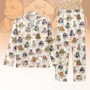 Könnte beinhalten: Cremefarbenes Pyjama-Set mit einem sich wiederholenden Muster von Cartoon-Katzen, die als Fantasy-Charaktere verkleidet sind. Das Set beinhaltet ein Hemd mit Knöpfen und eine passende Hose. Jede Katze ist mit einem Klassennamen wie "Warlock" oder "Ranger" versehen.