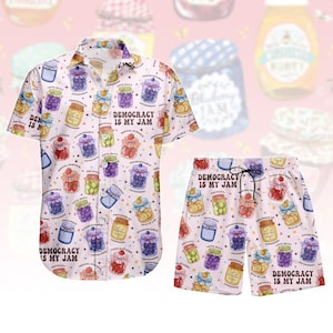 Könnte beinhalten: Ein zweiteiliges Set aus hellrosa Hemd und Shorts mit bunten Illustrationen von Marmeladengläsern mit verschiedenen Früchten und dem Text "DEMOCRACY IS MY JAM". Das Hemd ist kurzärmlig und hat Knöpfe.