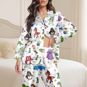 Könnte beinhalten: Weißes Pyjama-Set mit einem sich wiederholenden Muster aus Zeichentrickfiguren und goldenen Sternen. Das langärmlige Oberteil hat eine Knopfleiste und die Hose hat einen elastischen Bund. Das Pyjama-Set ist aus seidigem Material.