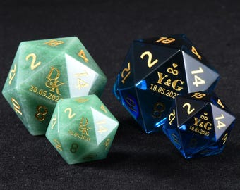 May include: Two green stone and two blue translucent twenty-sided dice featuring gold engraved numbers. The green dice are inscribed with D&K and 20.05.2025, while the blue dice feature Y&G with an infinity symbol and 18.05.2025.