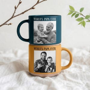 Peut inclure: Deux mugs en céramique empilés. Le mug supérieur est bleu sarcelle avec une photo en noir et blanc d'un homme et d'un enfant, avec le texte "WORLD'S. PAPA. EVER." Le mug inférieur est jaune.