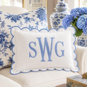 Peut inclure: Un coussin rectangulaire blanc avec un bord festonné garni de bleu clair. Le centre présente les lettres monogrammées brodées SWG en fil bleu clair. Le coussin a une texture de tissu lisse et une forme rectangulaire classique.