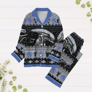 Könnte beinhalten: Blauer und schwarzer Pyjama-Set mit einem sich wiederholenden Muster einer weltraumthematischen Alien-Kreatur. Der Pyjama hat ein Oberteil mit Knöpfen und eine lange Hose.