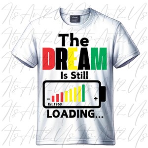 May include: White t-shirt with the text "The DREAM is Still Loading..." in black, red, green, and yellow. The text "Est. 1963" is below the loading bar graphic.
