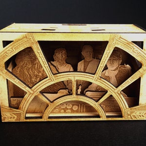 Op de afbeelding: Een houten doos met een uitgesneden ontwerp van een ruimteschipcockpit. De doos heeft vier figuren, waaronder een piloot, een copiloot en twee andere bemanningsleden. De figuren zijn gemaakt van hout en hebben een gedetailleerd ontwerp.