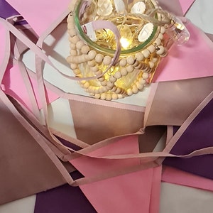 Könnte beinhalten: Ein rosa, lila und braunes Stoffbanner mit einem Glasgefäß gefüllt mit Holzperlen und Lichterketten.