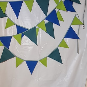Pode incluir: Uma bandeirola verde, azul e branca com bandeiras triangulares. A bandeirola está pendurada em uma parede branca.