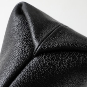May include: Close-up of a black leather bag corner. The leather has a textured grain and is stitched together at the corner. The bag appears to be new and unused.