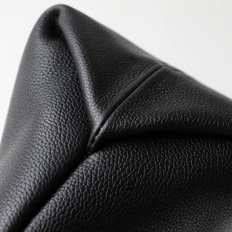 May include: Close-up of a black leather bag corner. The leather has a textured grain and is stitched together at the corner. The bag appears to be new and unused.