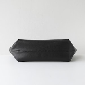 May include: A black leather tote bag with a rectangular shape. The bag has a textured surface and a stitched seam running across the center. The bag is set against a white background.