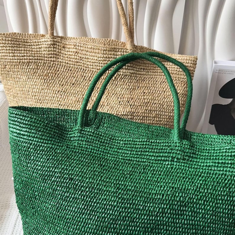 May include: Two large woven tote bags with sturdy handles. One bag is a natural tan color, and the other is a vibrant green. Both bags feature a textured, braided construction with an open top design, providing a spacious interior for carrying items.