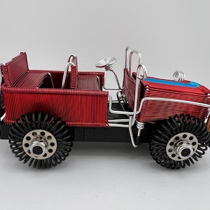 May include: A red wire-wrapped jeep with black wire wheels. The jeep has a blue stripe on the hood and a wire-wrapped bed.