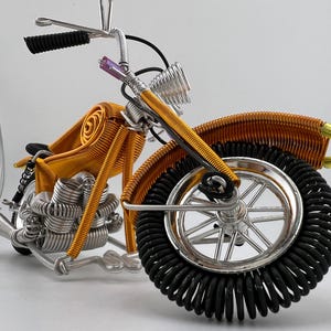 May include: A gold wire motorcycle sculpture with black wire wheels. The motorcycle has a detailed engine and handlebars.