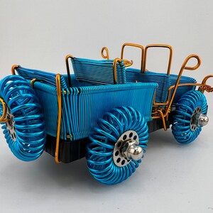 May include: A blue wire sculpture of a pickup truck with gold accents. The truck has a bed, a cab, and four wheels. The wheels are made of coiled wire.