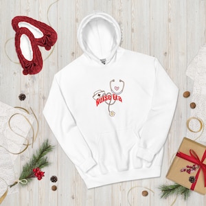 May include: White hoodie with a front pocket and a hood. The design features a nurse's hat, stethoscope, and the words "Nurse Era" in red. Red slippers are visible in the upper left corner.