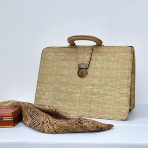 May include: A vintage briefcase with a woven texture, featuring a handle and clasp. A patterned scarf and a small wooden box with a clasp are also present. The items are arranged on a white surface.