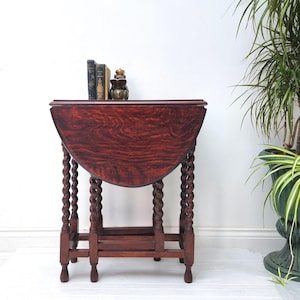 May include: A dark wood, drop-leaf table with a rounded top and twisted legs. The table is closed and has a shelf underneath.