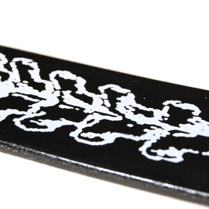 Op de afbeelding: Zwarte leren riem met een wit ontwerp van een herhalend patroon van bladeren.