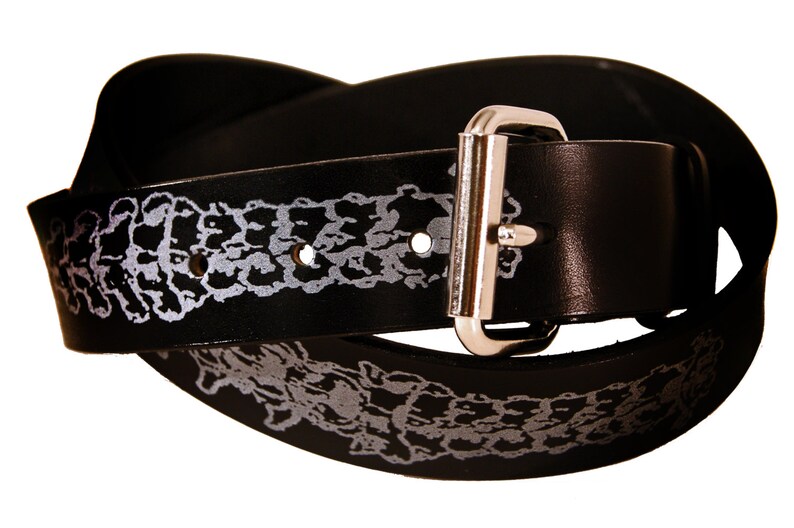 Op de afbeelding: Een zwarte leren riem met een zilveren gesp. De riem heeft een wit patroon.
