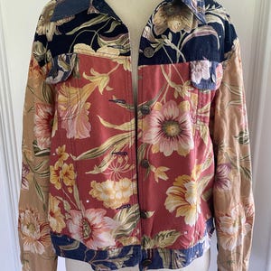 May include: A floral print jacket with a button-up front. The jacket features a mix of colors, including red, tan, navy, and yellow. The floral pattern is prominent, with large flowers and leaves. The jacket has a collared neckline and two front pockets.
