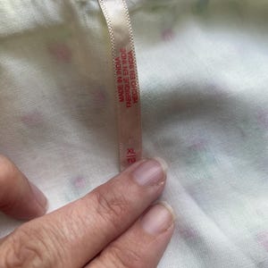 May include: Close-up of white fabric with a floral pattern in pink and green. A tag with the text "MADE IN INDIA" and size "XL" is attached to the fabric.