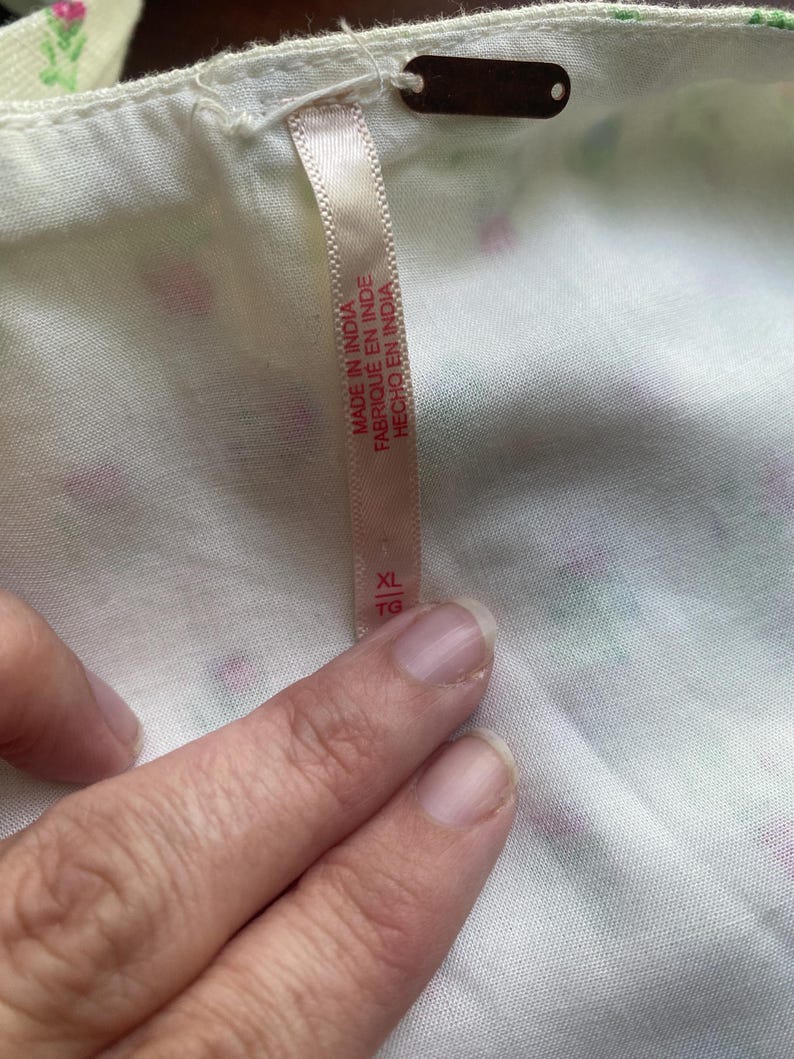 May include: Close-up of white fabric with a floral pattern in pink and green. A tag with the text "MADE IN INDIA" and size "XL" is attached to the fabric.