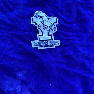 May include: Royal blue fabric with a white patch featuring a cougar and the text "BRIGHAM YOUNG UNIVERSITY". The cougar is in a leaping pose. The fabric has a soft, textured appearance.