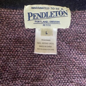 Puede incluir: Primer plano de un su&eacute;ter Pendleton morado y azul marino. La etiqueta dice "PENDLETON PORTLAND, OREGON PETITE" e incluye la talla "L". La etiqueta tambi&eacute;n indica que el su&eacute;ter es 100% lana merino y est&aacute; hecho en China.