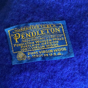 May include: Close-up of a vibrant blue textile with a sewn-on label. The label, in gold and blue, reads "PENDLETON WOOLEN MILLS" and "100% VIRGIN WOOL." The text also states "MADE IN U.S.A."