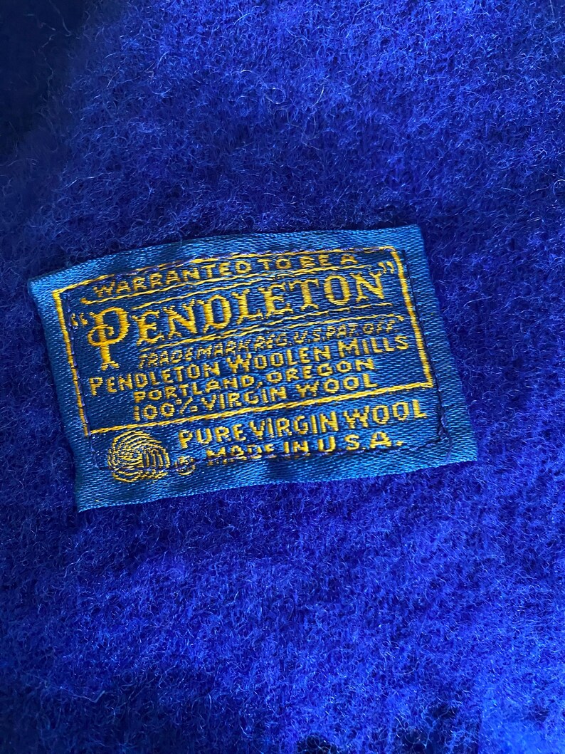 May include: Close-up of a vibrant blue textile with a sewn-on label. The label, in gold and blue, reads "PENDLETON WOOLEN MILLS" and "100% VIRGIN WOOL." The text also states "MADE IN U.S.A."
