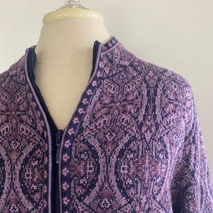 Puede incluir: Un c&aacute;rdigan con cremallera y estampado en tonos morados y azul marino. El intrincado dise&ntilde;o geom&eacute;trico cubre la parte delantera y las mangas. Tiene un cuello alto y una cremallera completa. La prenda se exhibe en un maniqu&iacute;.