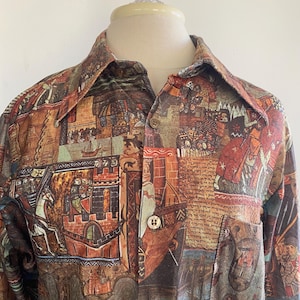 May include: A long-sleeved button-down shirt with a medieval tapestry print in shades of brown, orange, and red. The shirt features a collared neckline, a chest pocket, and gold-colored buttons. The fabric displays scenes of castles, battles, and figures.