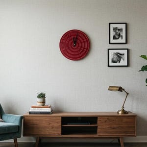 Puede incluir: Un salón moderno con un sillón turquesa, una consola de medios de madera y una gran planta en maceta. Un reloj rojo cuelga de la pared, junto con dos fotos en blanco y negro enmarcadas. Una lámpara de escritorio de latón está sobre la consola.